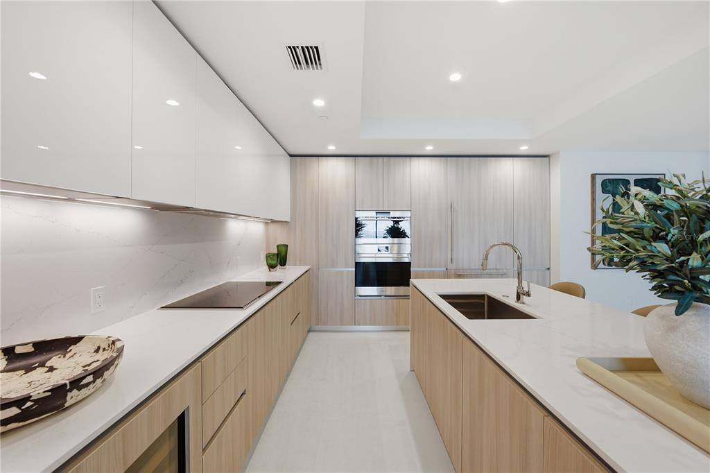 A modern kitchen features light wood cabinetry, white countertops, a central island, and integrated appliances — 5713 BOWEN DANIEL DRIVE UNIT 402, TAMPA, FL