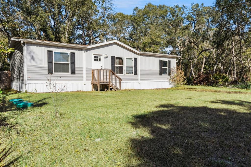 A single-story manufactured home with gray siding and a small wooden front porch — 231 TROPIC AVENUE, SATSUMA, FL