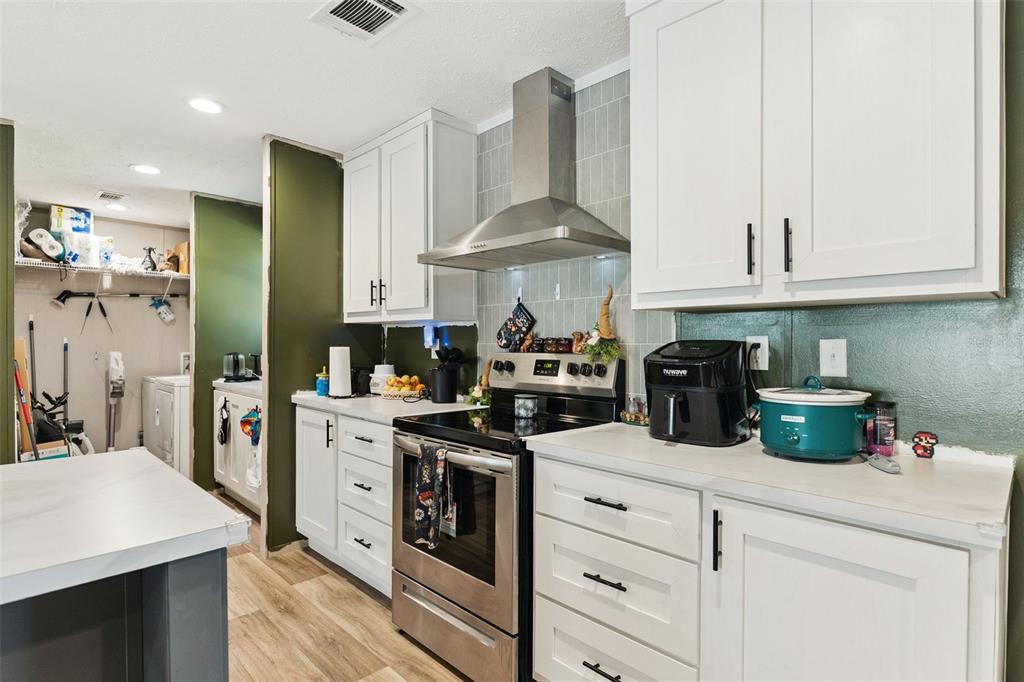 A kitchen features white cabinets, stainless steel appliances, and an adjacent utility area — 231 TROPIC AVENUE, SATSUMA, FL