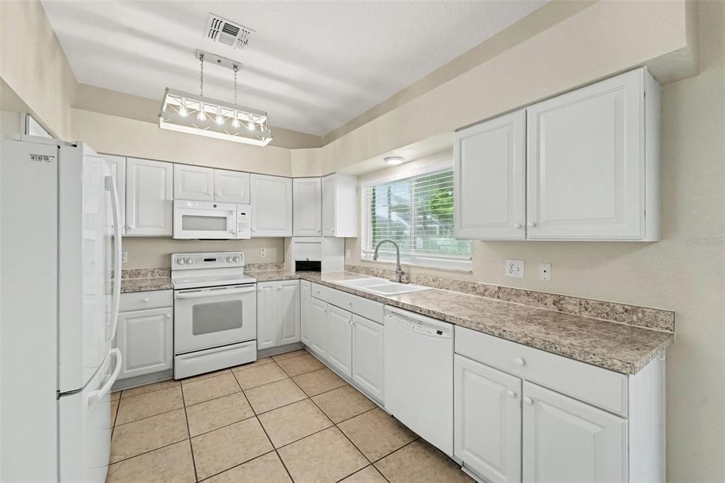A kitchen features white cabinets, laminate countertops, a white appliance suite, and tiled flooring — 19431 SANDY SPRINGS CIRCLE, LUTZ, FL