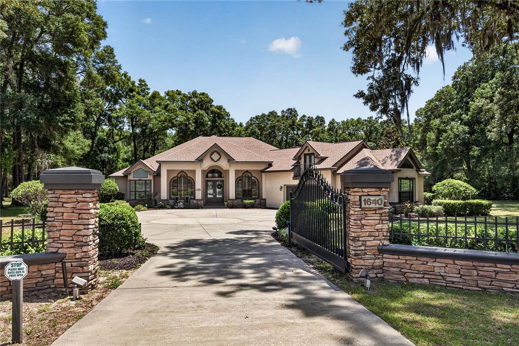A gated driveway leads to a single-story house with a stone wall and mature trees — 1640 SE 91ST PLACE, OCALA, FL