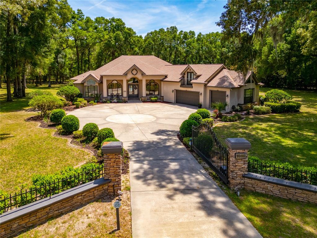 A single-story house with a gated driveway and stone wall sits behind a lush lawn — 1640 SE 91ST PLACE, OCALA, FL