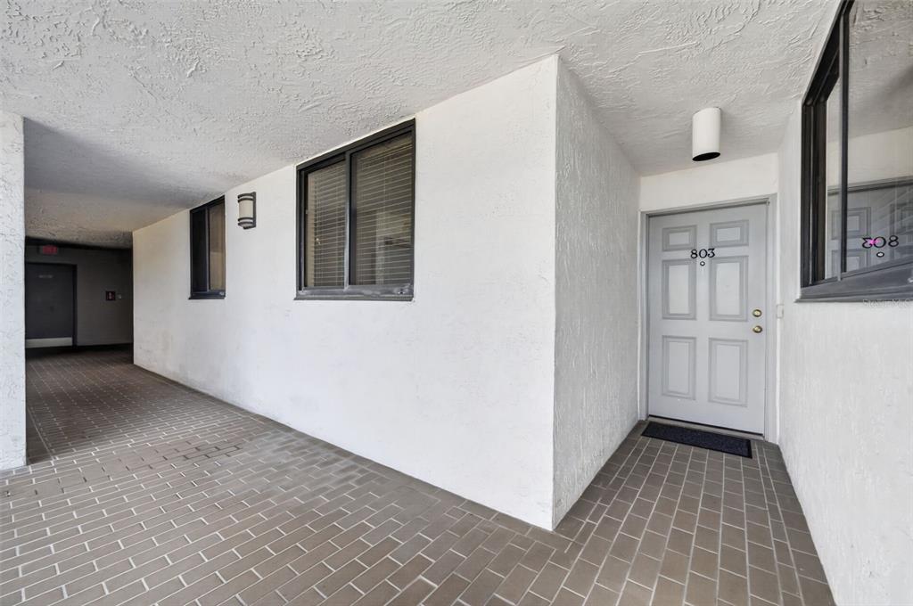 A white apartment door numbered 803 sits at the end of a covered brick walkway — 530 E CENTRAL BOULEVARD UNIT 803, ORLANDO, FL