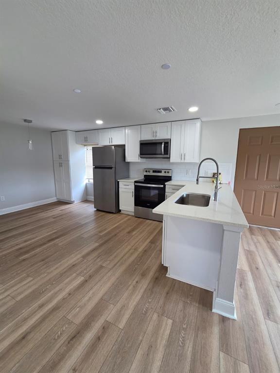 A kitchen features white cabinets, stainless steel appliances, a center island, and wood-look flooring — 300 ERON WAY UNIT 1, WINTER GARDEN, FL