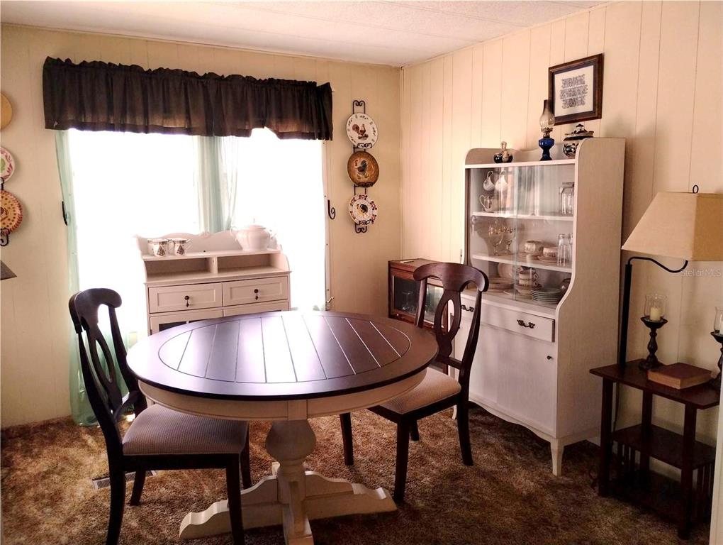 A dining room features a round table, two chairs, a hutch, and brown carpeting — 7409 SKYLINE DRIVE, HUDSON, FL