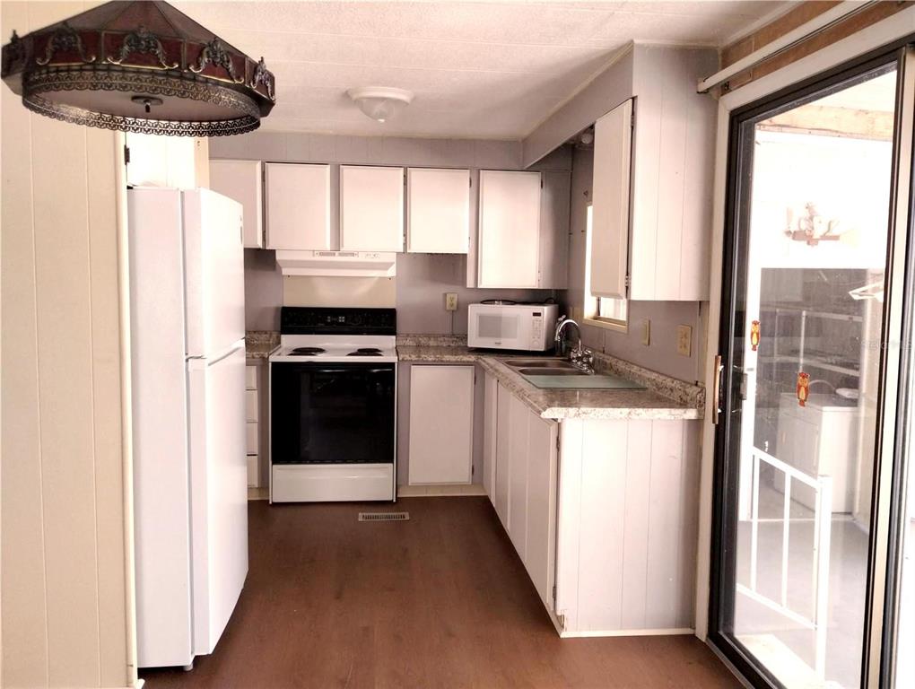 A kitchen features white cabinetry, a white stove, a refrigerator, and wood-look flooring — 7409 SKYLINE DRIVE, HUDSON, FL