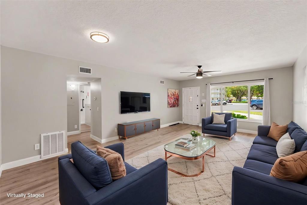 A living room with light wood floors, blue furniture, a television, and a large window — 2262 SWEDISH DRIVE UNIT 14, CLEARWATER, FL