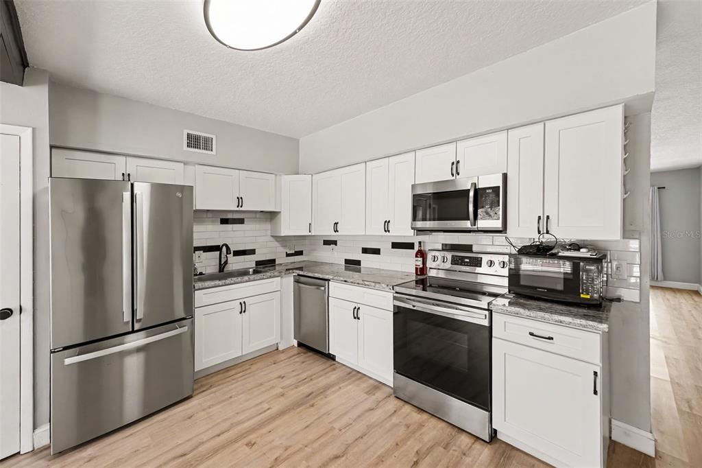 A kitchen features white cabinets, stainless steel appliances, a tiled backsplash, and light wood flooring — 2262 SWEDISH DRIVE UNIT 14, CLEARWATER, FL