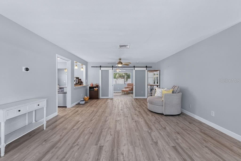 A living room features light gray walls, wood-look flooring, and sliding barn doors — 2159 GREENBRIAR BOULEVARD, CLEARWATER, FL