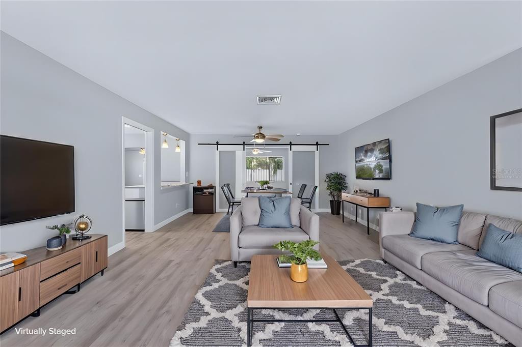 A living room with light gray walls, wood-look flooring, a ceiling fan, and a curved sofa — 2159 GREENBRIAR BOULEVARD, CLEARWATER, FL