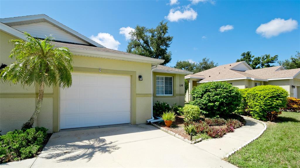 The exterior of a light-colored house features a white garage door and landscaped front yard — 209 28TH STREET W, PALMETTO, FL