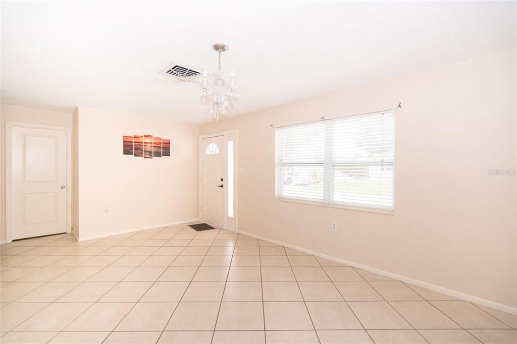 A bright, tiled entryway features a chandelier, a front door, and a multi-panel wall art — 8033 MANVEL DRIVE, PORT RICHEY, FL