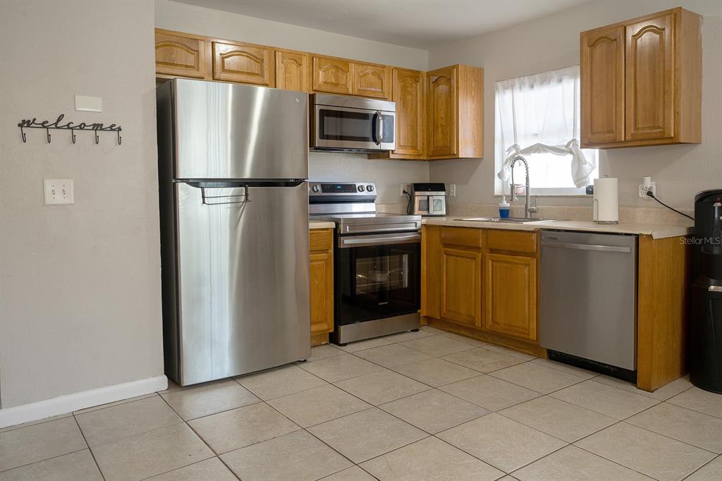 A kitchen features light wood cabinets, stainless steel appliances, and beige tile flooring — 3667 135TH AVENUE, LARGO, FL