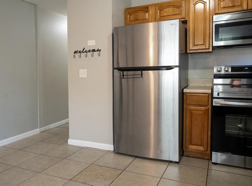 A kitchen features a stainless steel refrigerator, wooden cabinets, and tile flooring — 3667 135TH AVENUE, LARGO, FL