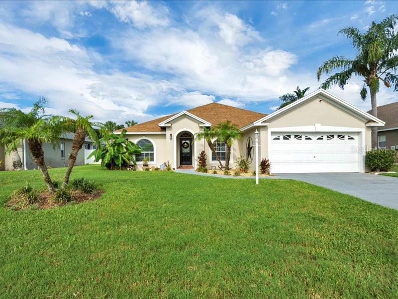 A single-story suburban house with a tan stucco exterior, a two-car garage, and palm trees — 344 RUBY LAKE LOOP, WINTER HAVEN, FL