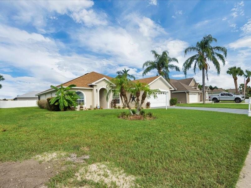 A single-story suburban house with a tan exterior, palm trees, and a green lawn — 344 RUBY LAKE LOOP, WINTER HAVEN, FL
