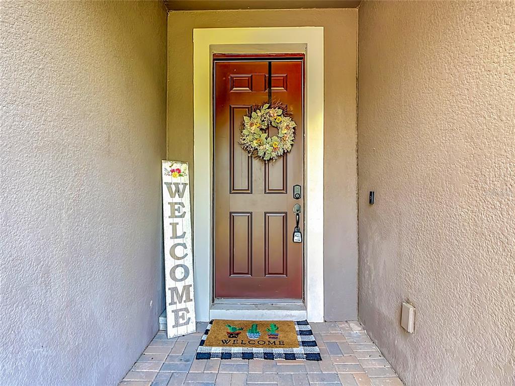 A bright entryway features a white door, tiled floors, a round mirror, and wall art — 2892 MATERA DRIVE, ST CLOUD, FL