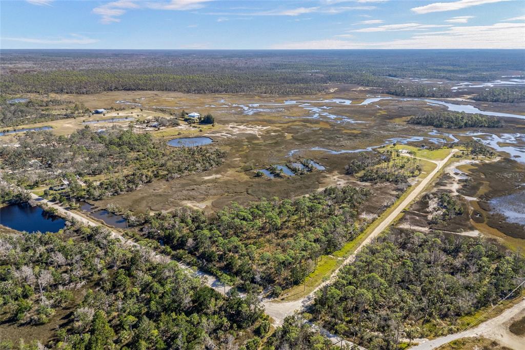 An aerial view shows a rural landscape with marshland, scattered trees, and a dirt road — 125 SW 284, STEINHATCHEE, FL