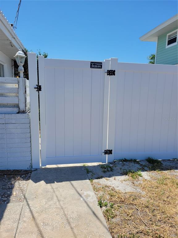 A white vinyl privacy fence with a gate stands next to a concrete walkway — 15318 HARBOR DRIVE, MADEIRA BEACH, FL