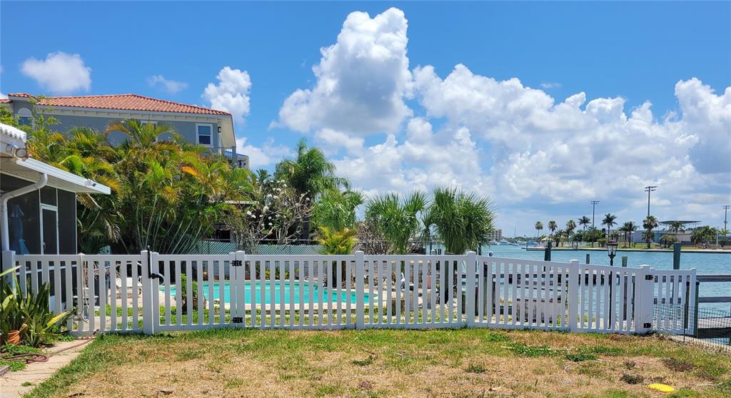 A white vinyl fence encloses a backyard with a swimming pool overlooking a waterfront canal — 15318 HARBOR DRIVE, MADEIRA BEACH, FL