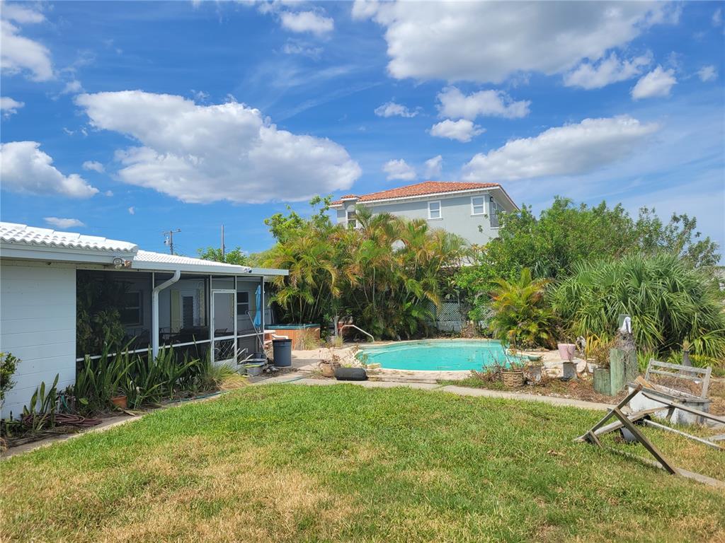 A backyard features a swimming pool, a screened-in patio, and lush landscaping under a blue sky — 15318 HARBOR DRIVE, MADEIRA BEACH, FL