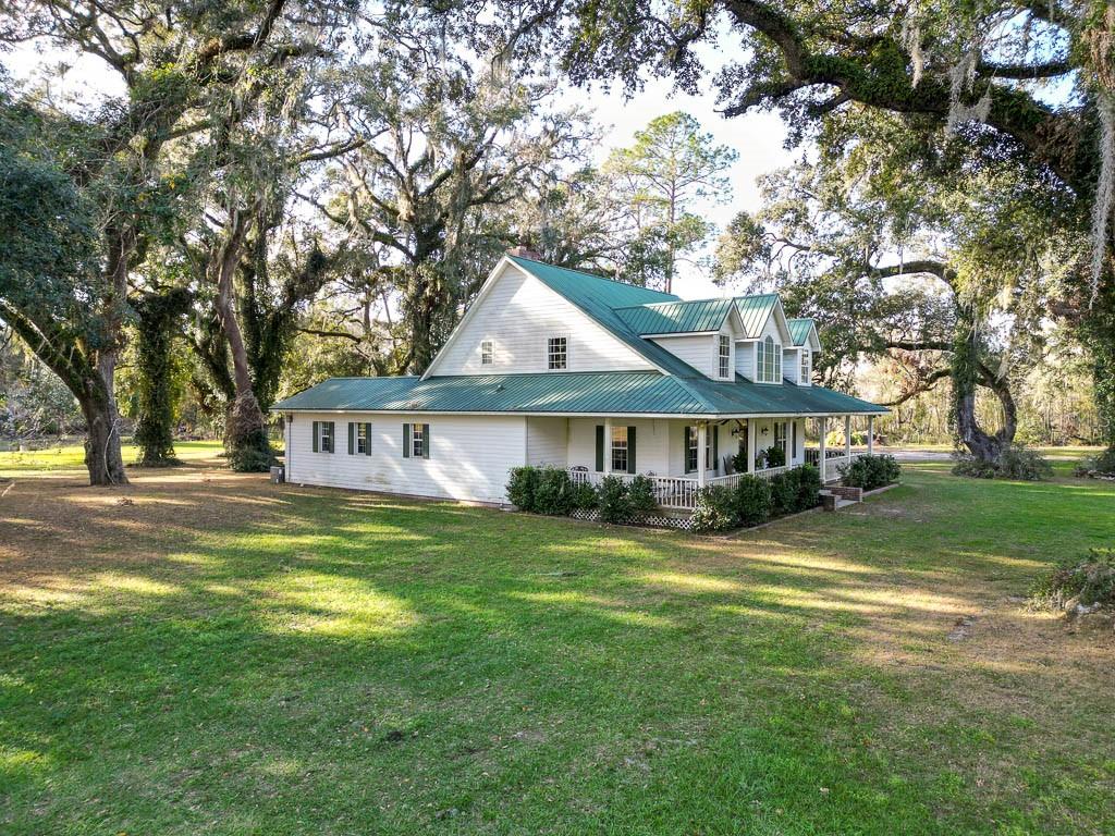 A white two-story house with a green metal roof sits on a grassy, tree-filled lot — 993 CR 722, WEBSTER, FL