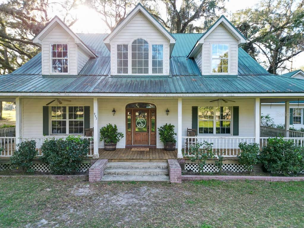 A white farmhouse with a green metal roof, a wrap-around porch, and three dormer windows — 993 CR 722, WEBSTER, FL