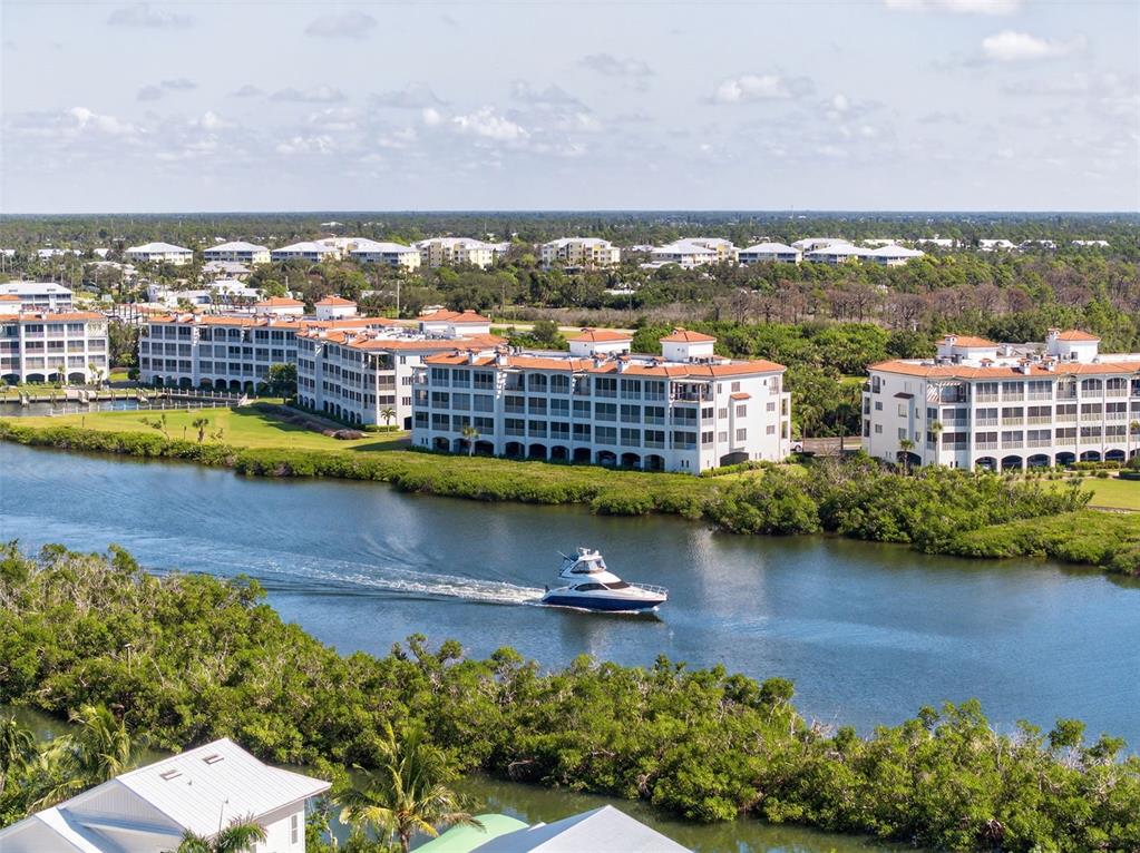 An aerial view shows a motorboat traveling on a waterway past multi-story residential buildings — 11120 HACIENDA DEL MAR BOULEVARD UNIT F-205, PLACIDA, FL