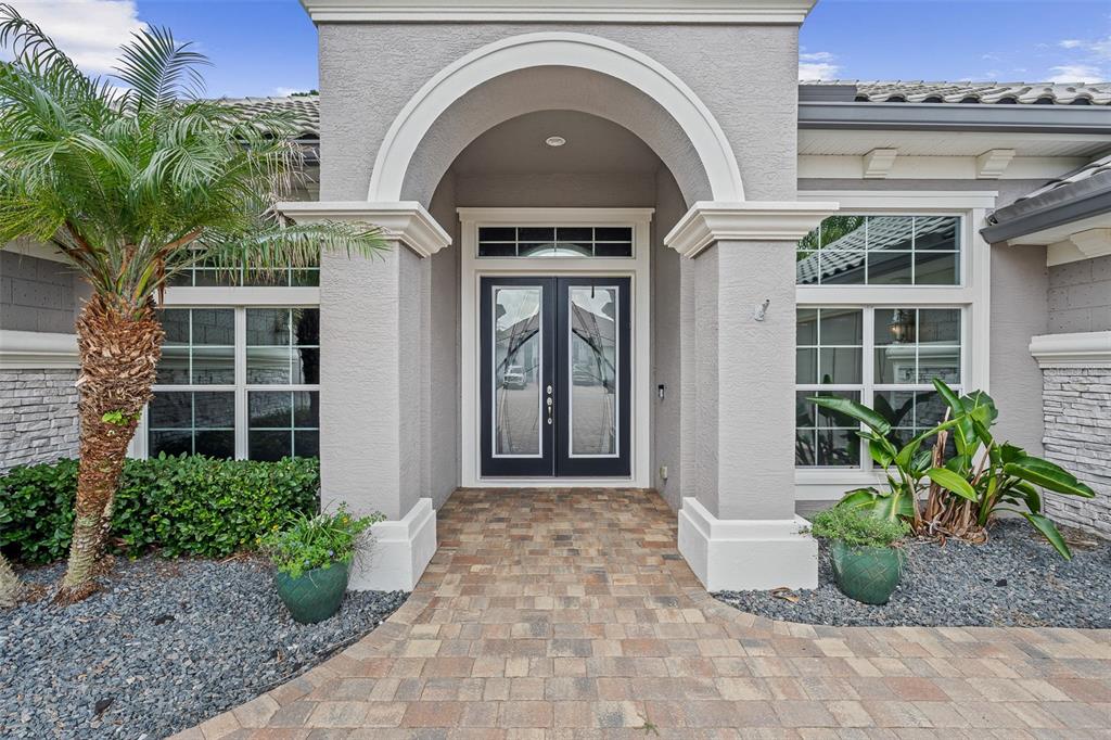 The front entrance of a house features a stone walkway, double glass doors, and landscaping — 630 WOODBRIDGE DRIVE, ORMOND BEACH, FL