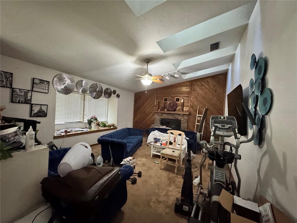 A living room features a brick fireplace with wood paneling, blue sofas, and a skylight — 713 NW 95TH TERRACE, GAINESVILLE, FL