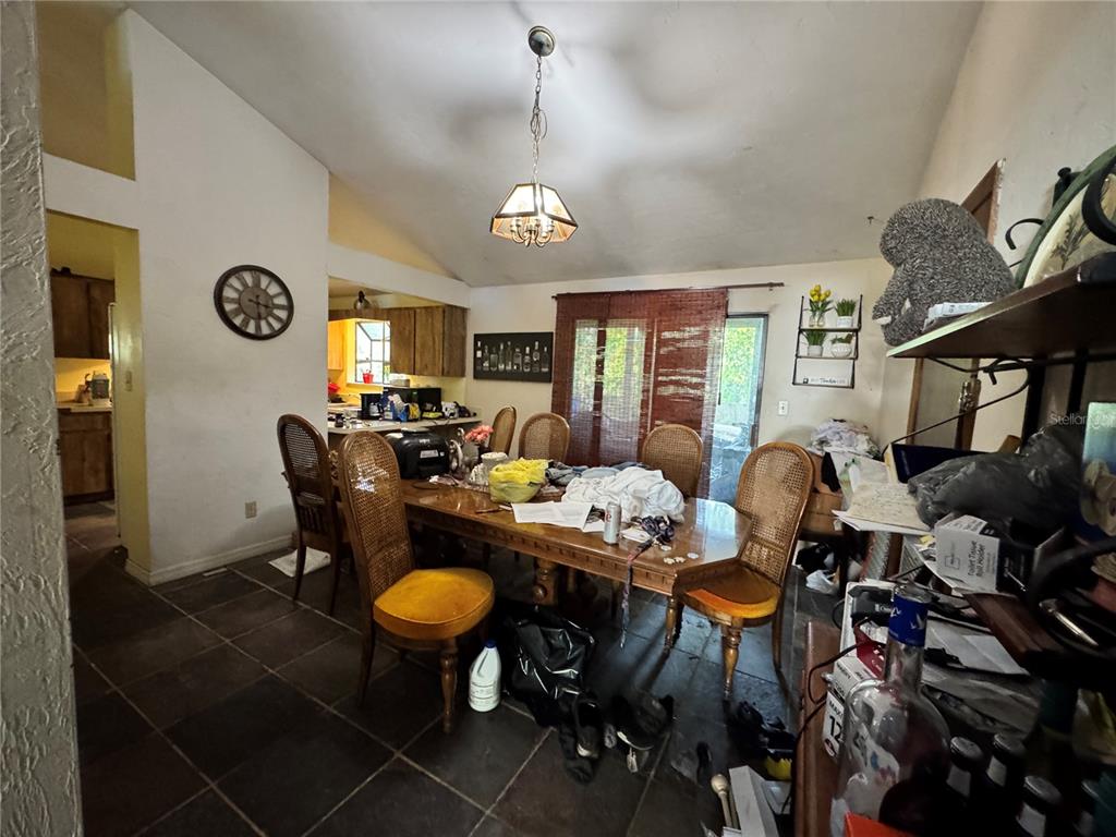 A dining room with a wooden table, cane-back chairs, tile flooring, and a vaulted ceiling — 713 NW 95TH TERRACE, GAINESVILLE, FL