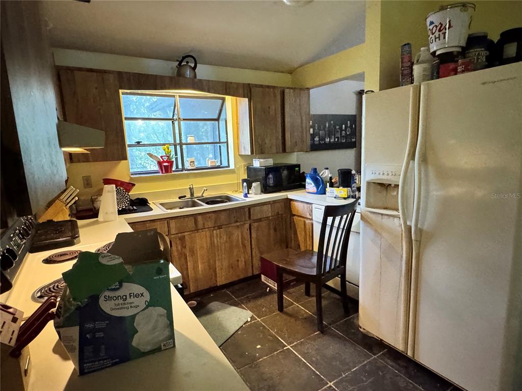 A kitchen with wood cabinets, a double sink, a white refrigerator, and a dark tile floor — 713 NW 95TH TERRACE, GAINESVILLE, FL