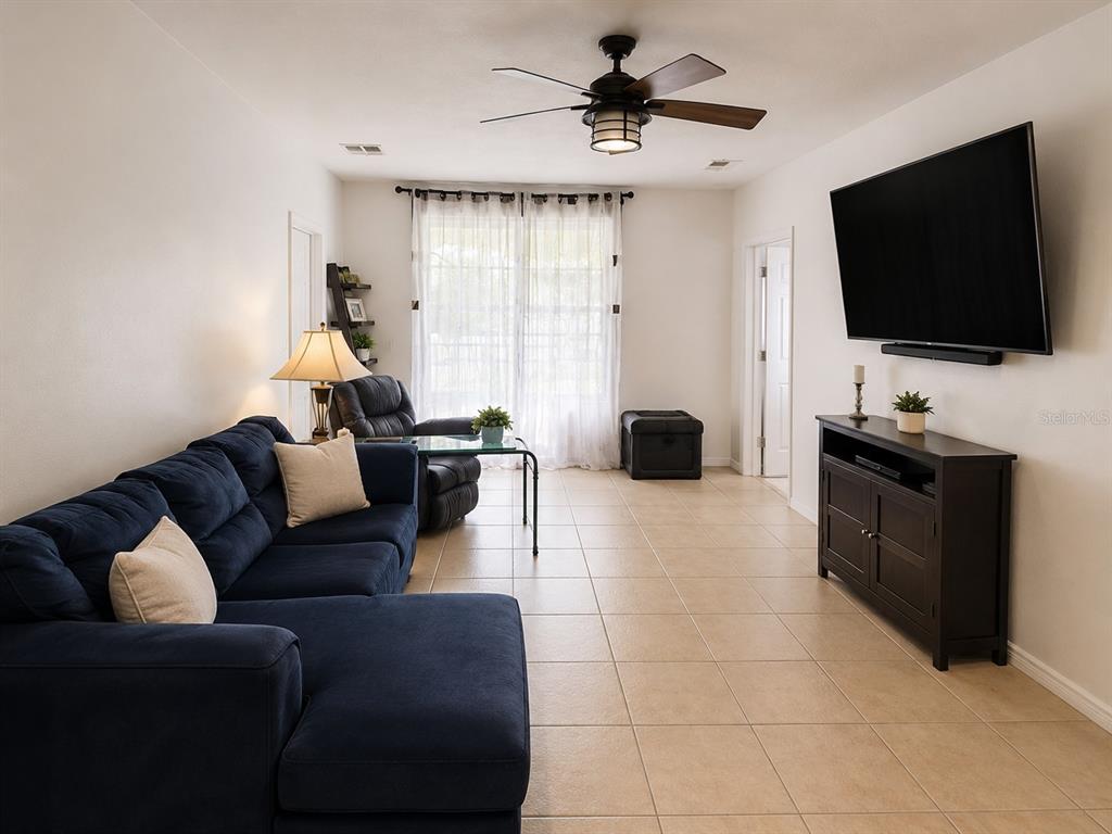 A living room features a blue sectional sofa, a wall-mounted television, and tile flooring — 318 SIGMUND LOOP, DAVENPORT, FL