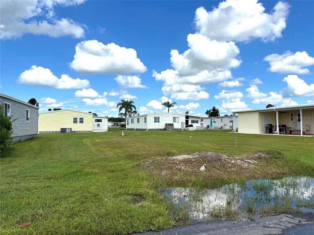 A grassy lot with a puddle in the foreground and several manufactured homes nearby — 626 LA SALA, NORTH PORT, FL