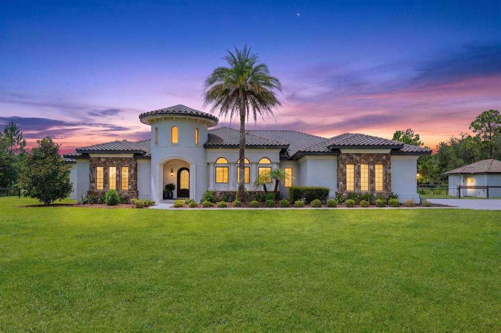 A single-story house with a stone facade, arched entryway, and a palm tree at sunset — 4156 BENEDICT AVENUE, ORLANDO, FL