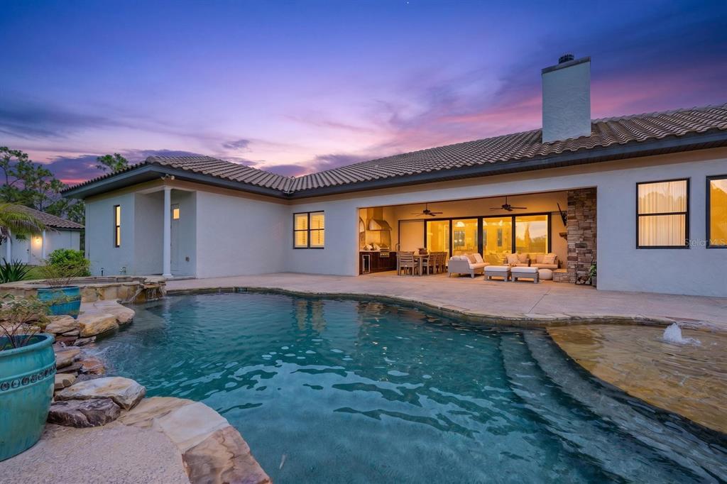 A swimming pool with a stone border sits in front of a house with a patio — 4156 BENEDICT AVENUE, ORLANDO, FL