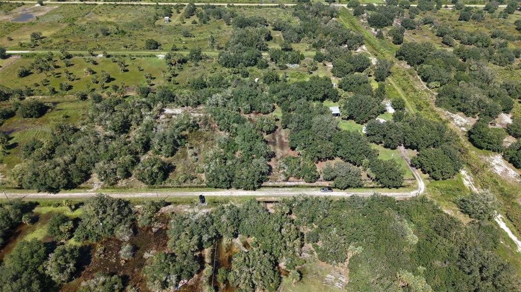 An aerial view shows a rural property with dense trees, a dirt road, and small structures — 20125 NW 300TH STREET, OKEECHOBEE, FL
