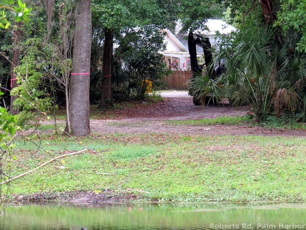 A dirt driveway leads toward a house partially obscured by trees and a construction vehicle — ROBERTS ROAD, PALM HARBOR, FL