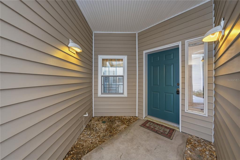 A covered entryway features beige horizontal siding, a teal front door, and two wall-mounted lights — 22128 LITTLE LAGOON COURT, LUTZ, FL