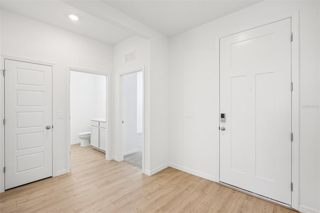 An interior view of a white-walled entryway featuring light wood flooring and three white doors — 4665 BARBERRY AVENUE, LAKELAND, FL