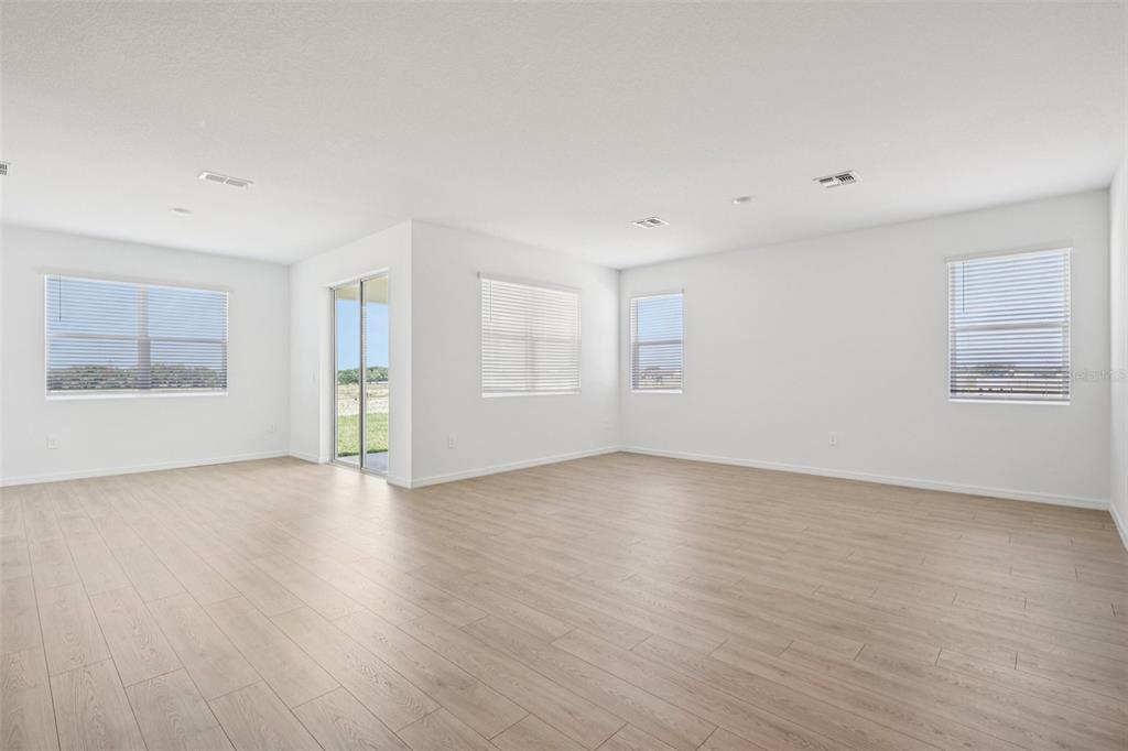 A bright, empty living room features light wood-look flooring, white walls, and multiple windows — 4665 BARBERRY AVENUE, LAKELAND, FL