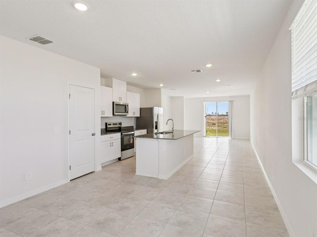 An open-concept kitchen features white cabinets, granite countertops, stainless steel appliances, and tile flooring — 729 IMPALA ROAD, LAKE ALFRED, FL
