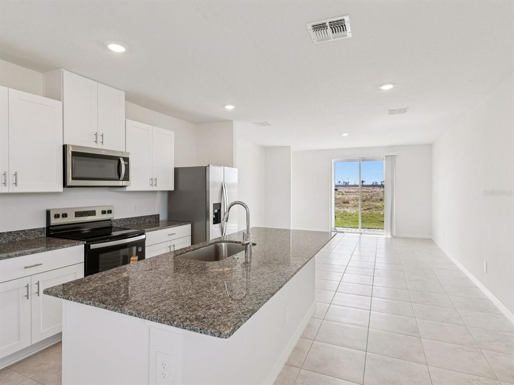 A kitchen with white cabinets, granite countertops, a center island, and tile flooring — 729 IMPALA ROAD, LAKE ALFRED, FL