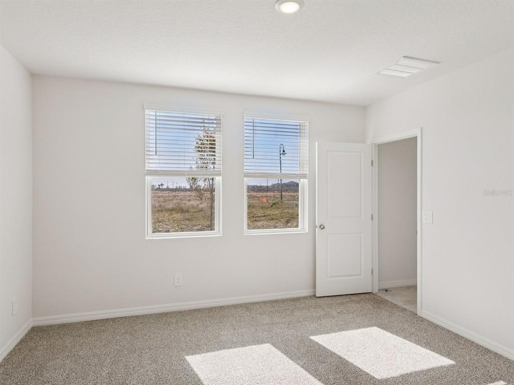 An empty bedroom with white walls, beige carpet, two windows, and an open doorway — 729 IMPALA ROAD, LAKE ALFRED, FL