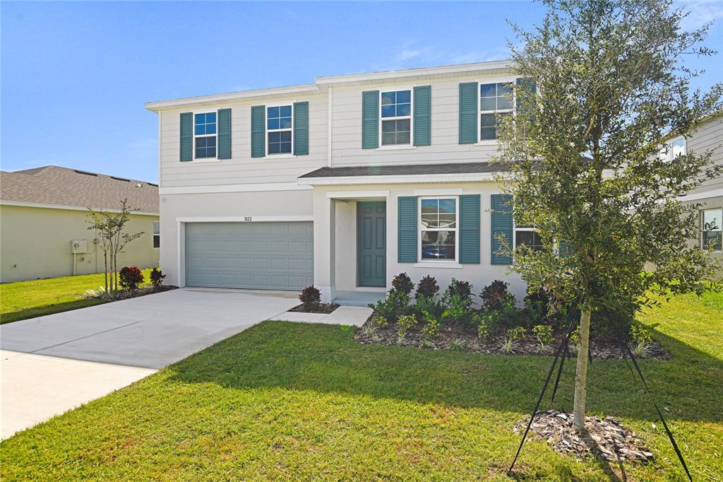 A two-story suburban house with a gray garage, teal shutters, and a landscaped front yard — 1022 WISTERIA WAY, DUNDEE, FL