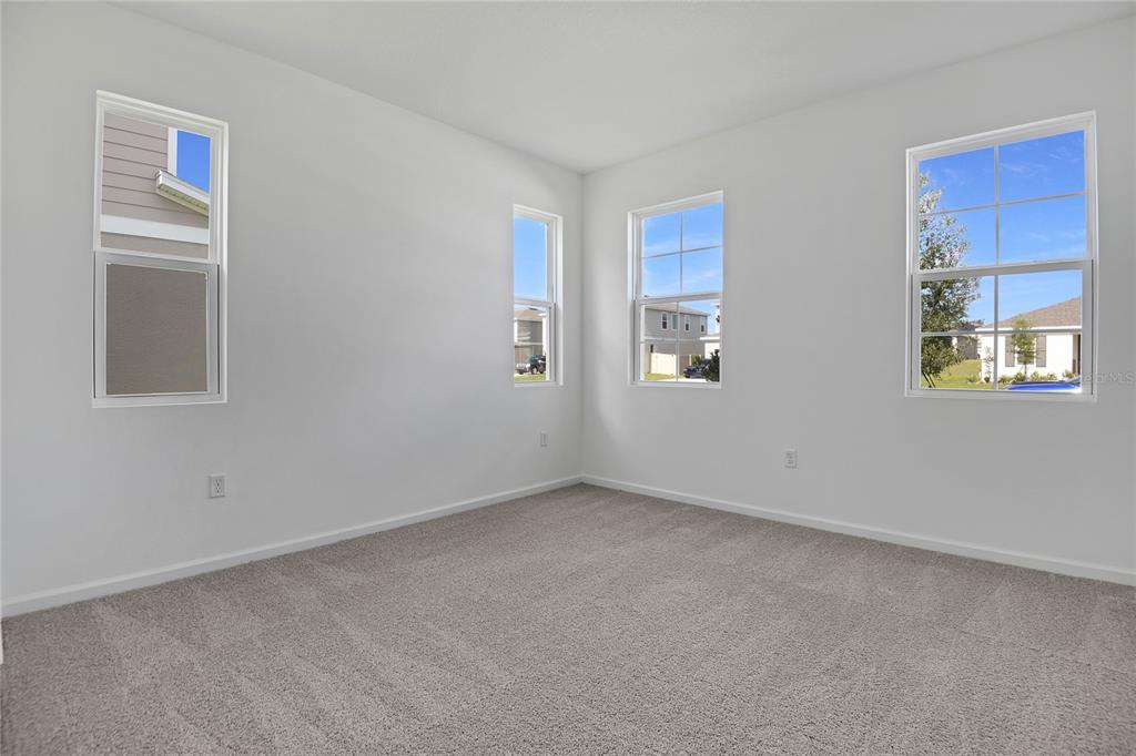 An empty bedroom features white walls, gray carpet, and four windows with views of neighboring houses — 1022 WISTERIA WAY, DUNDEE, FL
