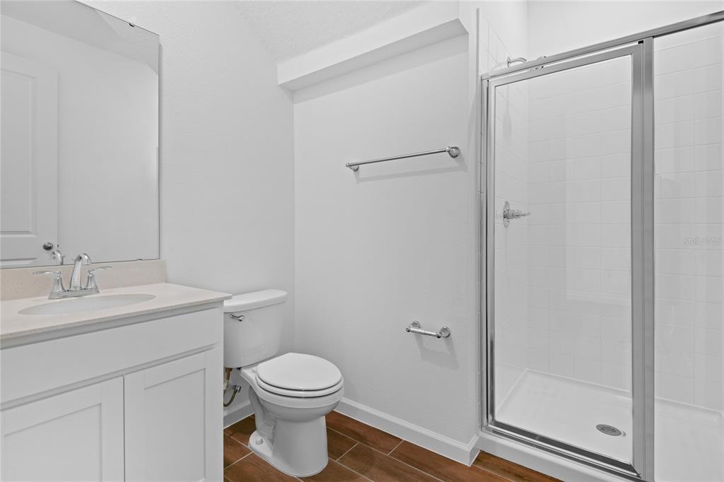A bathroom features a white vanity, a toilet, and a glass-enclosed shower with tiled walls — 1022 WISTERIA WAY, DUNDEE, FL