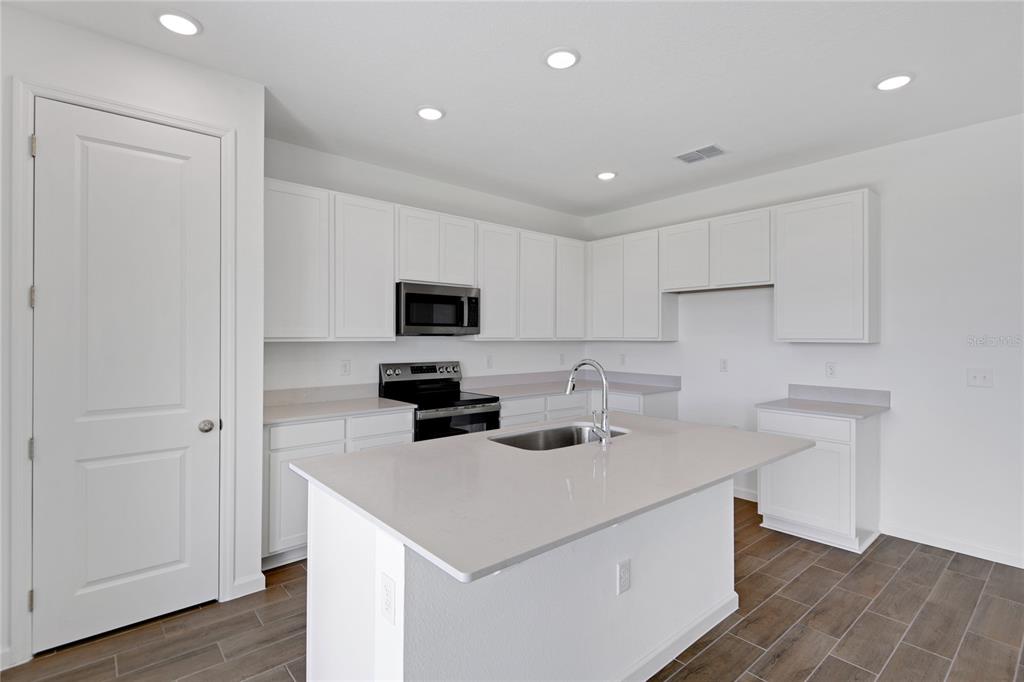 A modern kitchen features white cabinets, a central island with a sink, and wood-look flooring — 1022 WISTERIA WAY, DUNDEE, FL