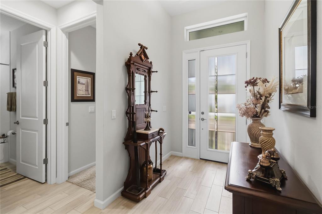 A bright entryway features light wood-look tile flooring, a white front door, and antique furniture — 1212 VICTORIA HILLS DRIVE N, DELAND, FL