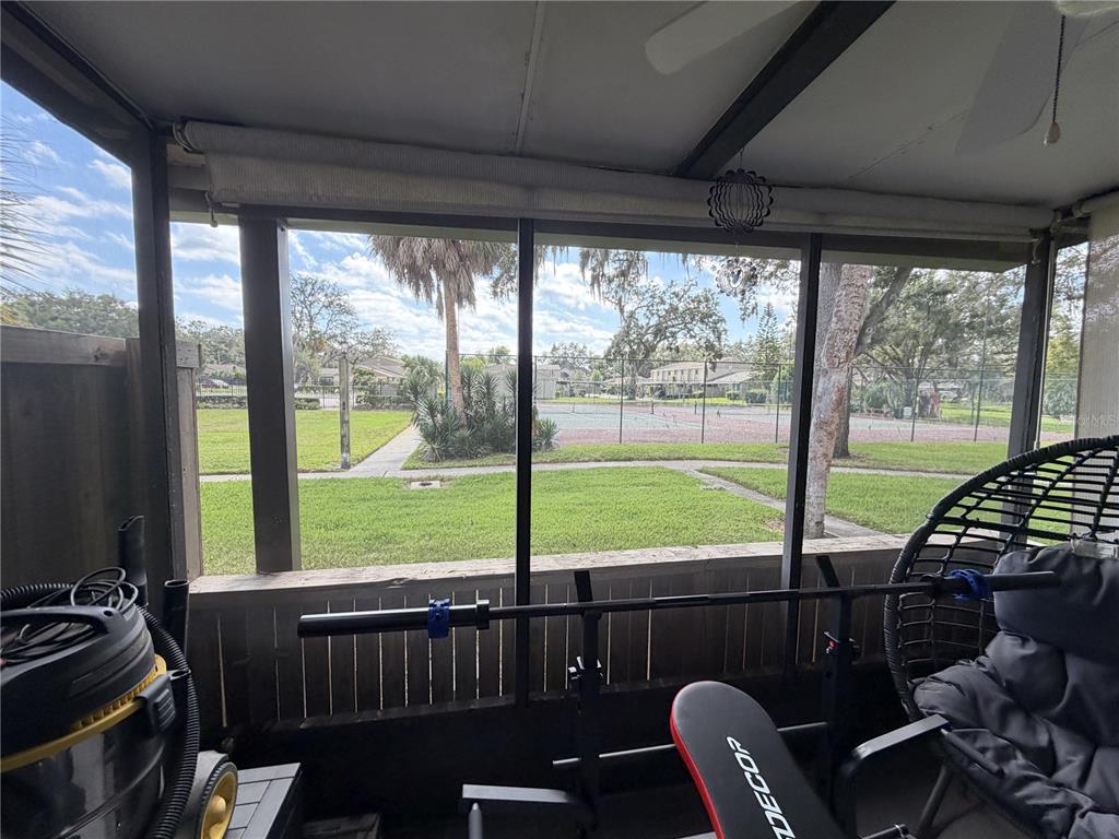 A screened-in porch overlooks a grassy area and a fenced tennis court — 7925 PINE DRIVE UNIT 33, TEMPLE TERRACE, FL